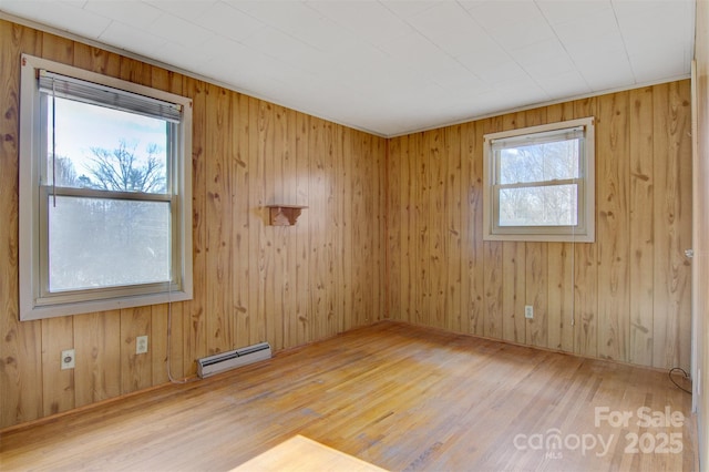 unfurnished room featuring hardwood / wood-style flooring, a wealth of natural light, and a baseboard heating unit