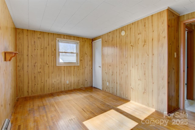 unfurnished room featuring wood-type flooring, wooden walls, and baseboard heating