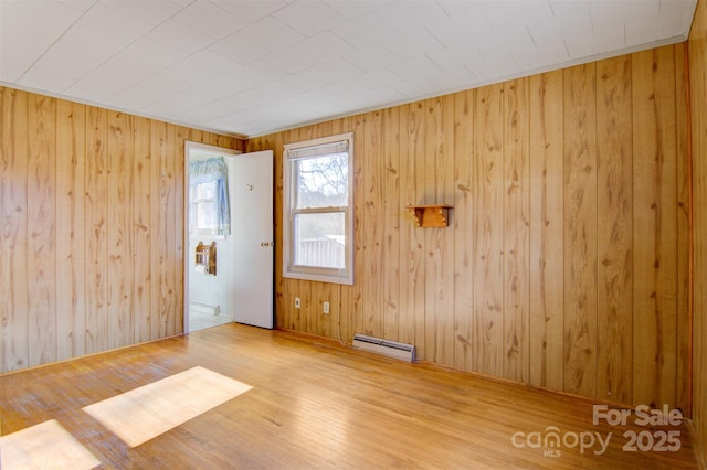 unfurnished room featuring wooden walls and baseboard heating