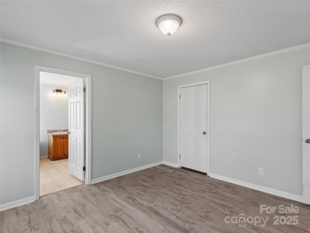 unfurnished bedroom featuring ornamental molding, ensuite bath, a textured ceiling, and light hardwood / wood-style flooring