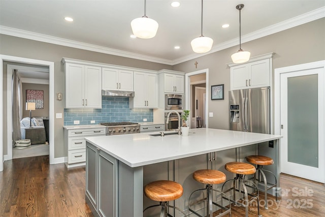 kitchen featuring white cabinetry, stainless steel appliances, decorative backsplash, a center island with sink, and decorative light fixtures