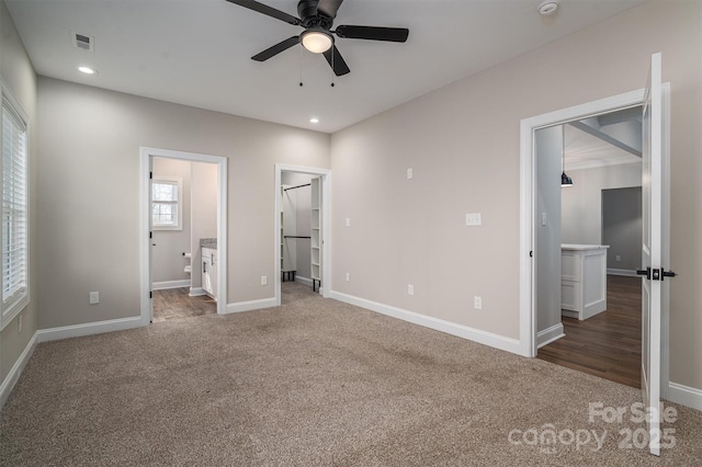 unfurnished bedroom with ceiling fan, dark colored carpet, connected bathroom, a spacious closet, and a closet