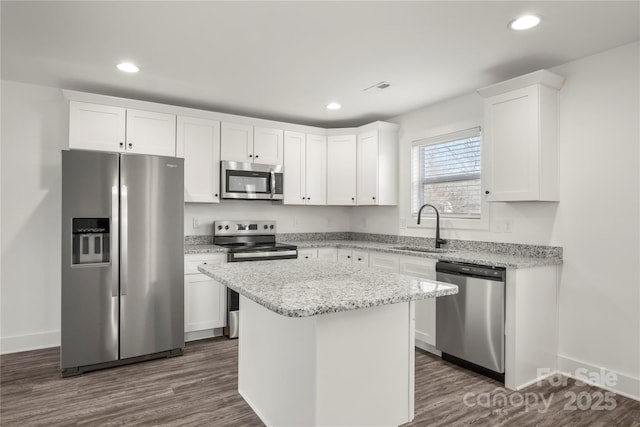 kitchen with sink, appliances with stainless steel finishes, light stone counters, white cabinets, and a kitchen island