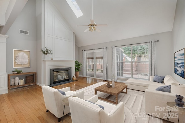 living room featuring ceiling fan, high vaulted ceiling, light hardwood / wood-style floors, and a skylight