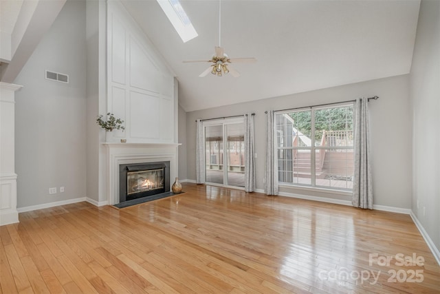 unfurnished living room featuring ceiling fan, a skylight, high vaulted ceiling, and light wood-type flooring