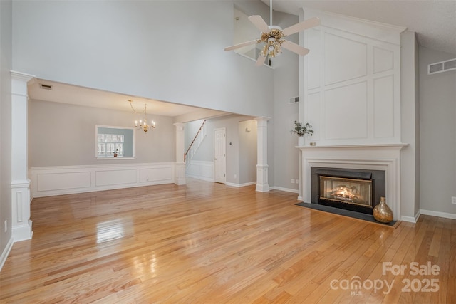 unfurnished living room featuring ornate columns, a high ceiling, ceiling fan with notable chandelier, and light hardwood / wood-style flooring