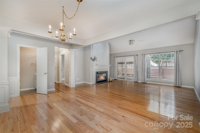 unfurnished living room with ornate columns, an inviting chandelier, a textured ceiling, and light hardwood / wood-style floors