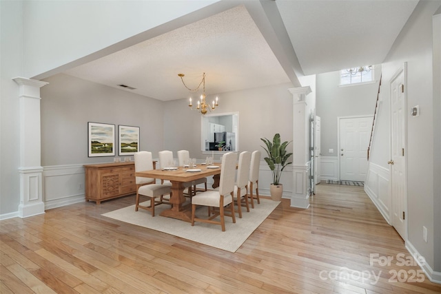 dining area with light hardwood / wood-style flooring, decorative columns, and a chandelier