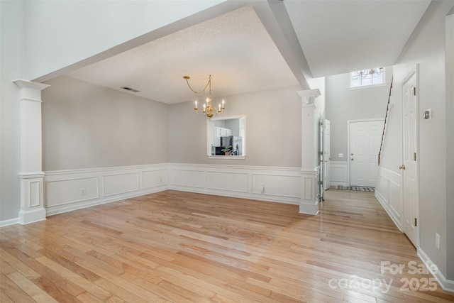 unfurnished room with decorative columns, a chandelier, and light hardwood / wood-style flooring