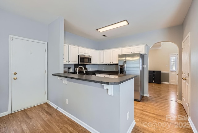 kitchen with white cabinetry, a kitchen breakfast bar, stainless steel appliances, kitchen peninsula, and light wood-type flooring