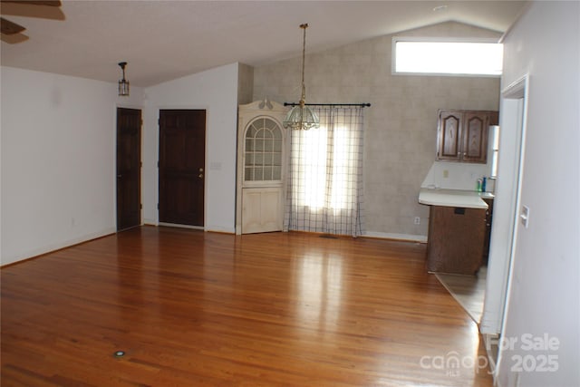 unfurnished dining area featuring hardwood / wood-style flooring, lofted ceiling, and ceiling fan with notable chandelier