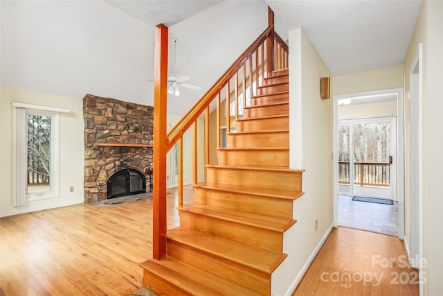 stairway featuring ceiling fan, wood-type flooring, a stone fireplace, and a textured ceiling