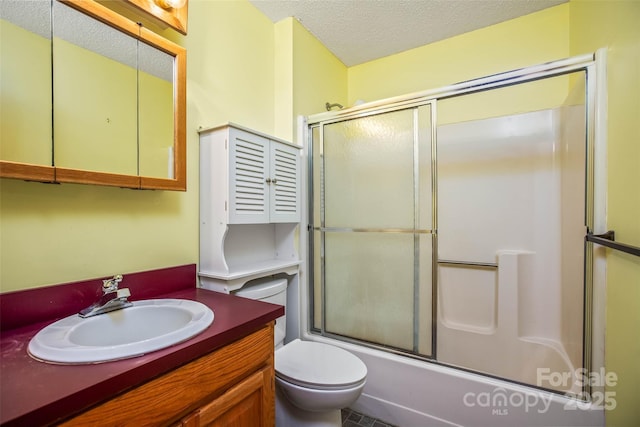 full bathroom featuring vanity, bath / shower combo with glass door, toilet, and a textured ceiling