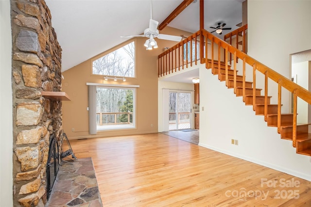 unfurnished living room with beam ceiling, wood-type flooring, a stone fireplace, and ceiling fan