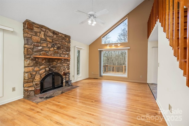 unfurnished living room with a stone fireplace, light hardwood / wood-style flooring, high vaulted ceiling, and ceiling fan