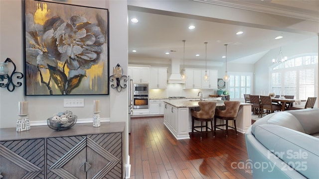 kitchen with a breakfast bar, light stone counters, white cabinets, a center island with sink, and decorative light fixtures