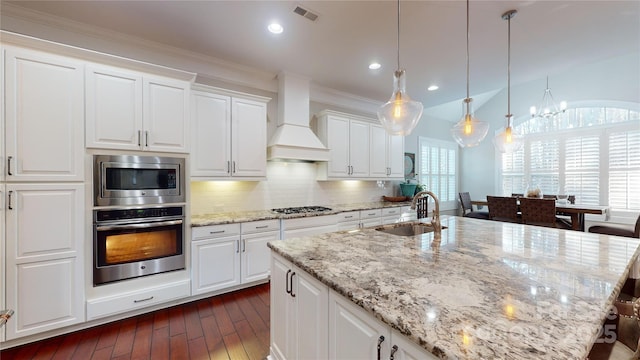 kitchen with sink, premium range hood, white cabinetry, appliances with stainless steel finishes, and decorative light fixtures