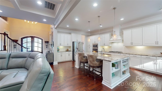 kitchen with decorative light fixtures, an island with sink, white cabinets, and appliances with stainless steel finishes