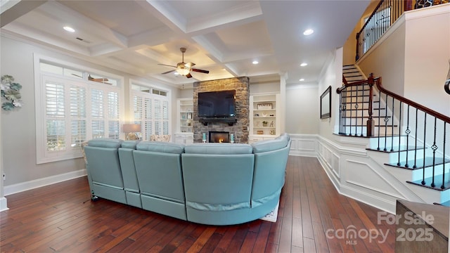 living room with built in shelves, coffered ceiling, a stone fireplace, dark hardwood / wood-style floors, and beamed ceiling