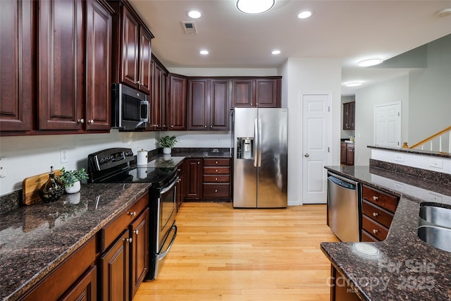 kitchen with stainless steel appliances, sink, light hardwood / wood-style floors, and dark stone counters