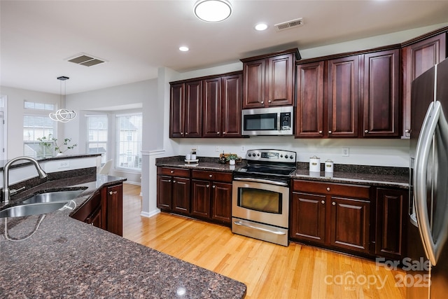 kitchen with pendant lighting, sink, dark stone countertops, stainless steel appliances, and light hardwood / wood-style flooring