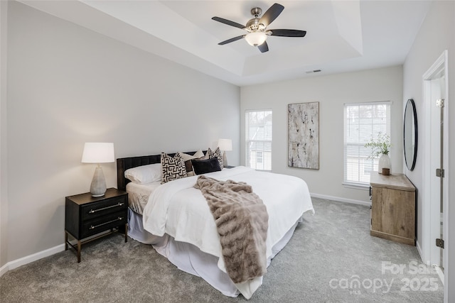 carpeted bedroom with a raised ceiling and ceiling fan