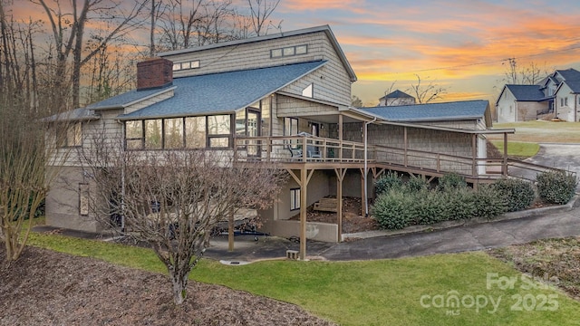 back house at dusk featuring a wooden deck and a lawn