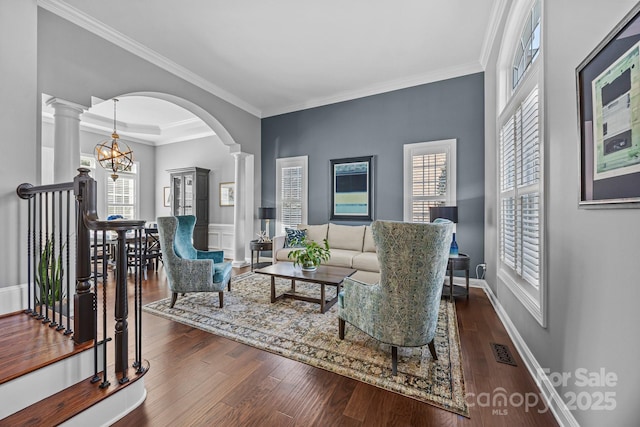 living room with an inviting chandelier, crown molding, decorative columns, and a raised ceiling