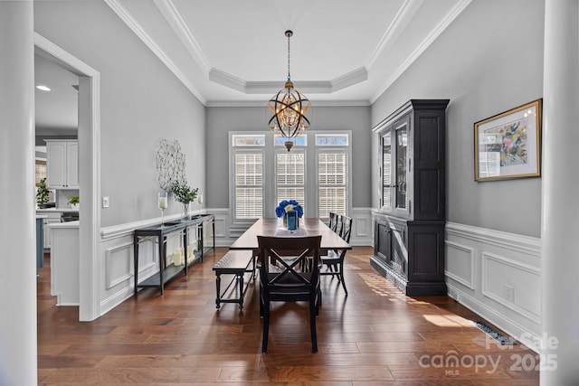 dining space with an inviting chandelier, crown molding, dark wood-type flooring, and a tray ceiling