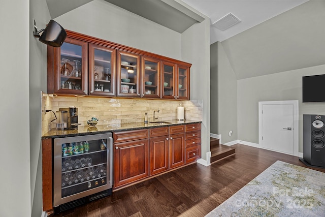 bar featuring sink, backsplash, dark hardwood / wood-style floors, beverage cooler, and dark stone counters