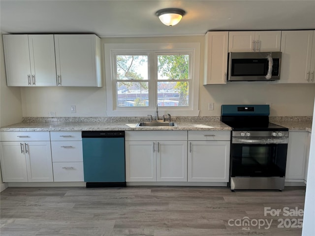 kitchen featuring sink, white cabinetry, light stone counters, light wood-type flooring, and appliances with stainless steel finishes