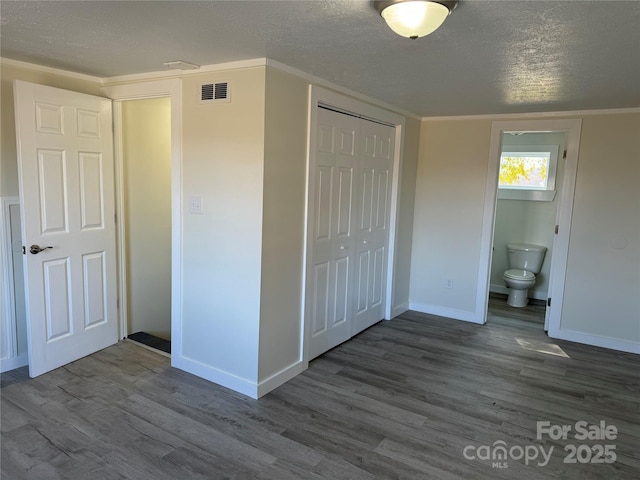 unfurnished bedroom with ensuite bathroom, dark hardwood / wood-style flooring, a closet, and a textured ceiling