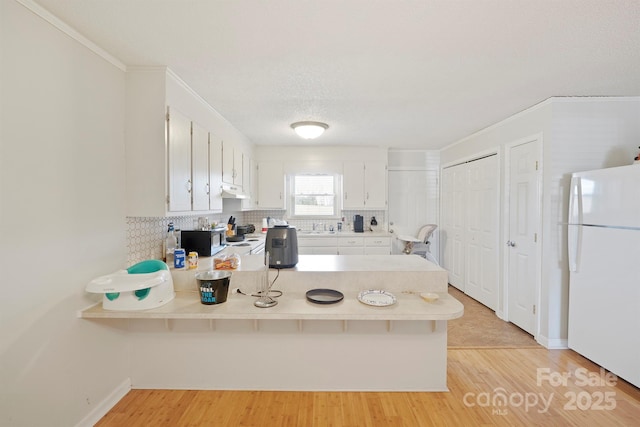 kitchen featuring white cabinets, decorative backsplash, white refrigerator, kitchen peninsula, and light wood-type flooring