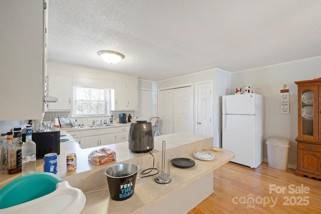 kitchen featuring sink, light hardwood / wood-style flooring, white cabinetry, white refrigerator, and a textured ceiling