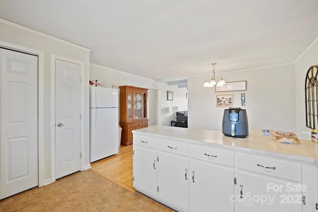 kitchen with hanging light fixtures, white fridge, white cabinets, and a textured ceiling