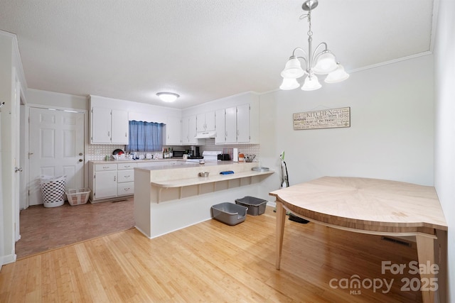 kitchen featuring hanging light fixtures, kitchen peninsula, light hardwood / wood-style floors, decorative backsplash, and white cabinets