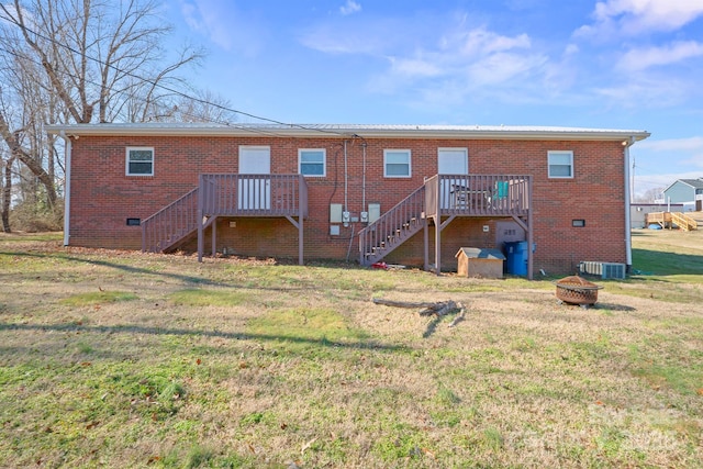 back of house with central air condition unit, a fire pit, and a lawn