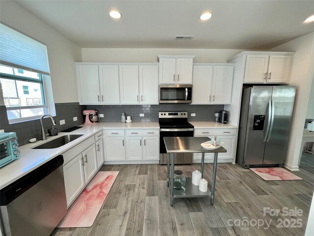 kitchen featuring sink, tasteful backsplash, appliances with stainless steel finishes, light hardwood / wood-style floors, and white cabinets