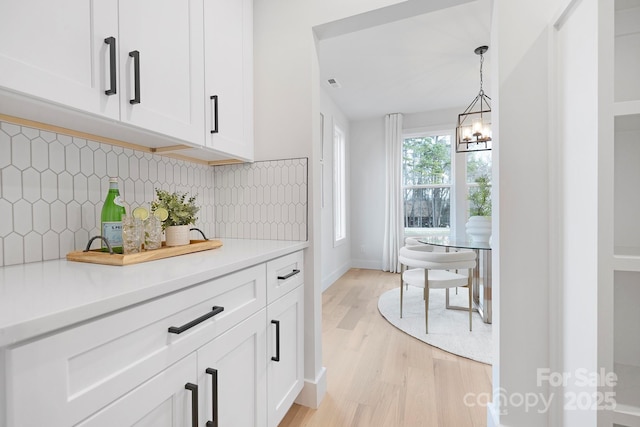 kitchen featuring white cabinets, decorative light fixtures, light hardwood / wood-style floors, and backsplash