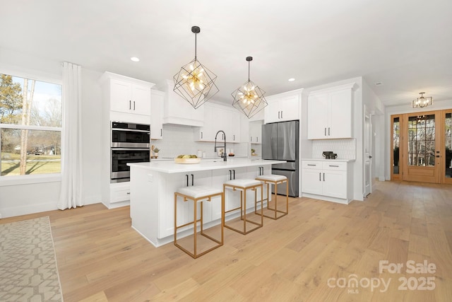 kitchen featuring white cabinetry, decorative backsplash, a kitchen island with sink, and appliances with stainless steel finishes