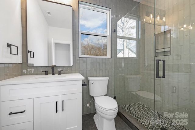 bathroom with tile walls, tile patterned flooring, vanity, a shower with shower door, and toilet