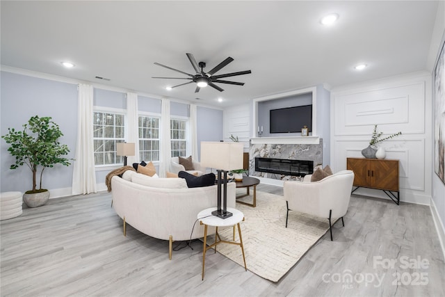 living room featuring crown molding, a premium fireplace, ceiling fan, and light wood-type flooring