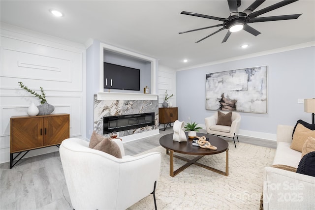 living room featuring hardwood / wood-style flooring, ceiling fan, a fireplace, and crown molding