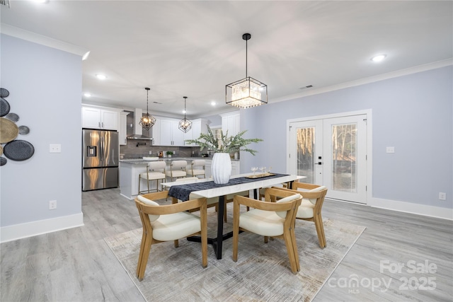 dining space with crown molding, light hardwood / wood-style floors, and french doors