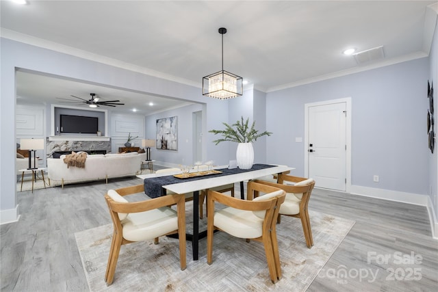 dining space with ornamental molding, ceiling fan, a high end fireplace, and light hardwood / wood-style flooring