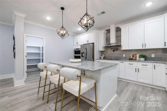 kitchen featuring wall chimney range hood, white cabinetry, stainless steel appliances, a center island, and a kitchen bar