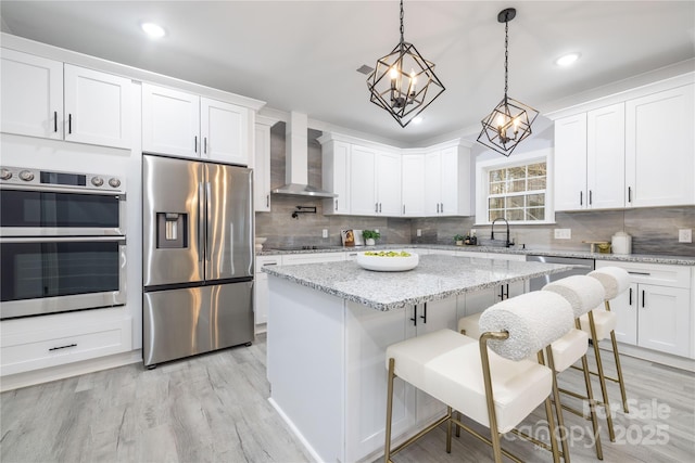 kitchen with wall chimney exhaust hood, appliances with stainless steel finishes, a kitchen breakfast bar, and white cabinets