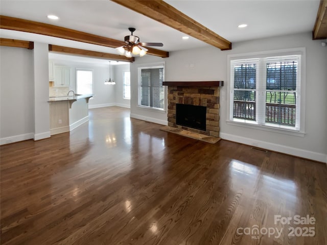 unfurnished living room with ceiling fan, beamed ceiling, a fireplace, and a healthy amount of sunlight