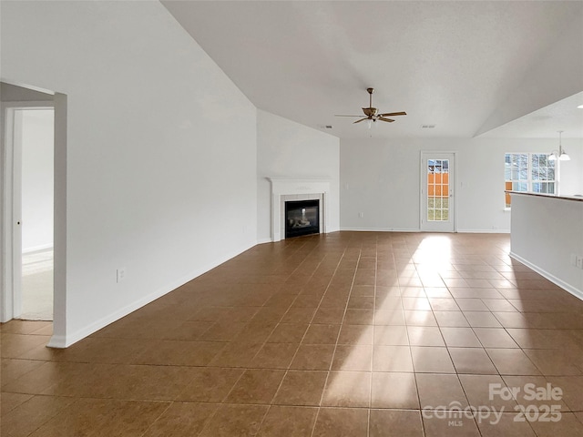 unfurnished living room featuring dark tile patterned flooring, ceiling fan with notable chandelier, a fireplace, and vaulted ceiling