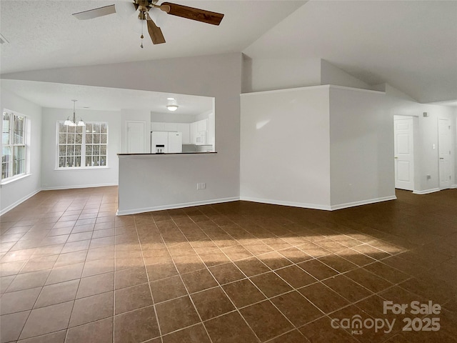 unfurnished living room featuring ceiling fan with notable chandelier, dark tile patterned flooring, and vaulted ceiling